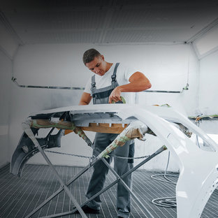 Prozesswärme Fahrzeuglackierer klebt eine weiße Stoßstange auf einem Ständer in der Lackierkabine ab